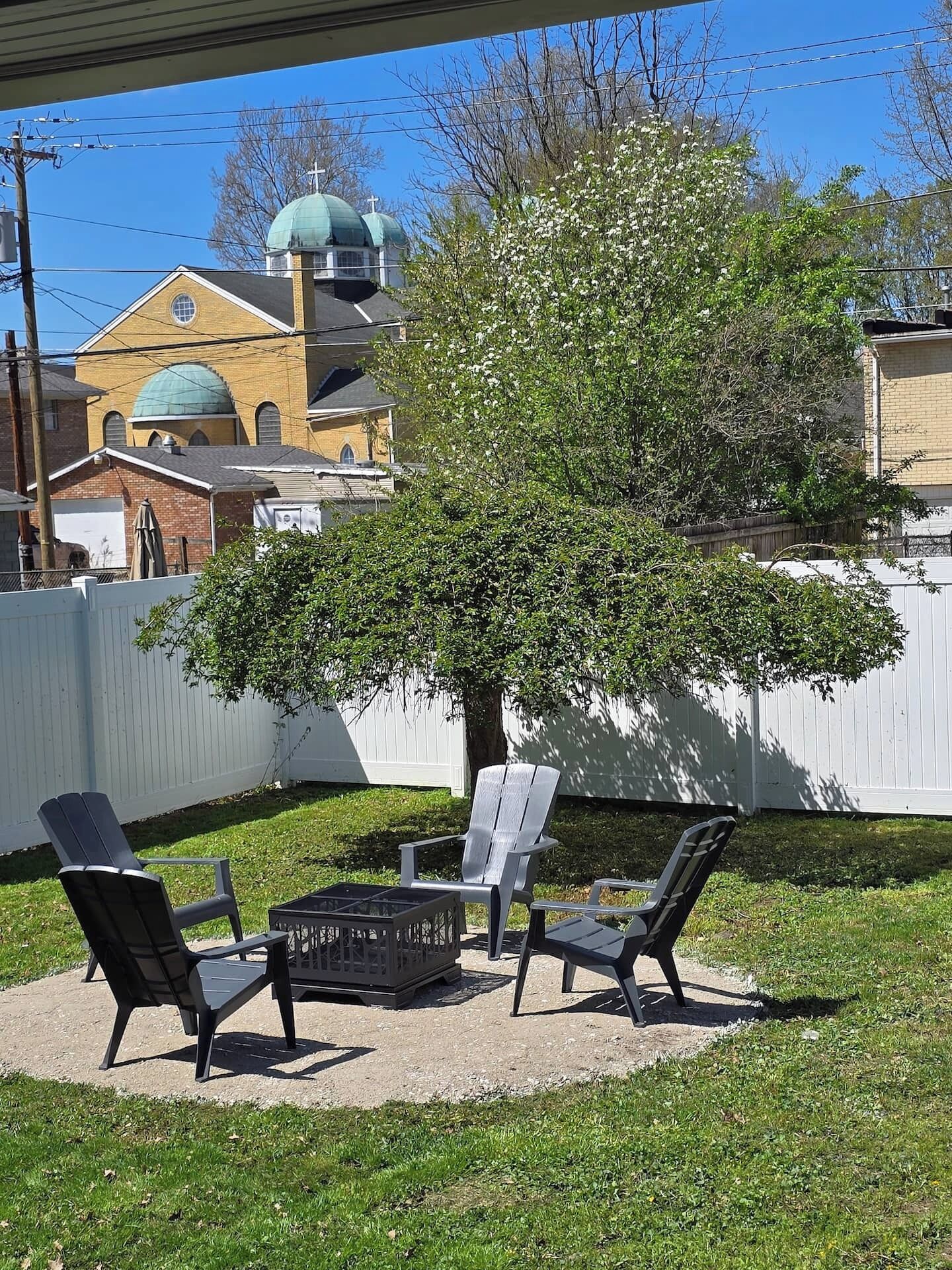 Ein Außenbereich mit Sitzgelegenheiten, einem Tisch, einem Baum und einem Gebäude mit einer grünen Kuppel im Hintergrund.
