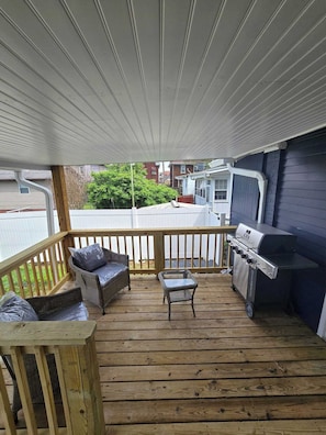 A covered deck with a grill, wicker furniture, and a view of the neighborhood. - The Park House  A 5 Bedroom Retreat w/Game Room & (Huntington)