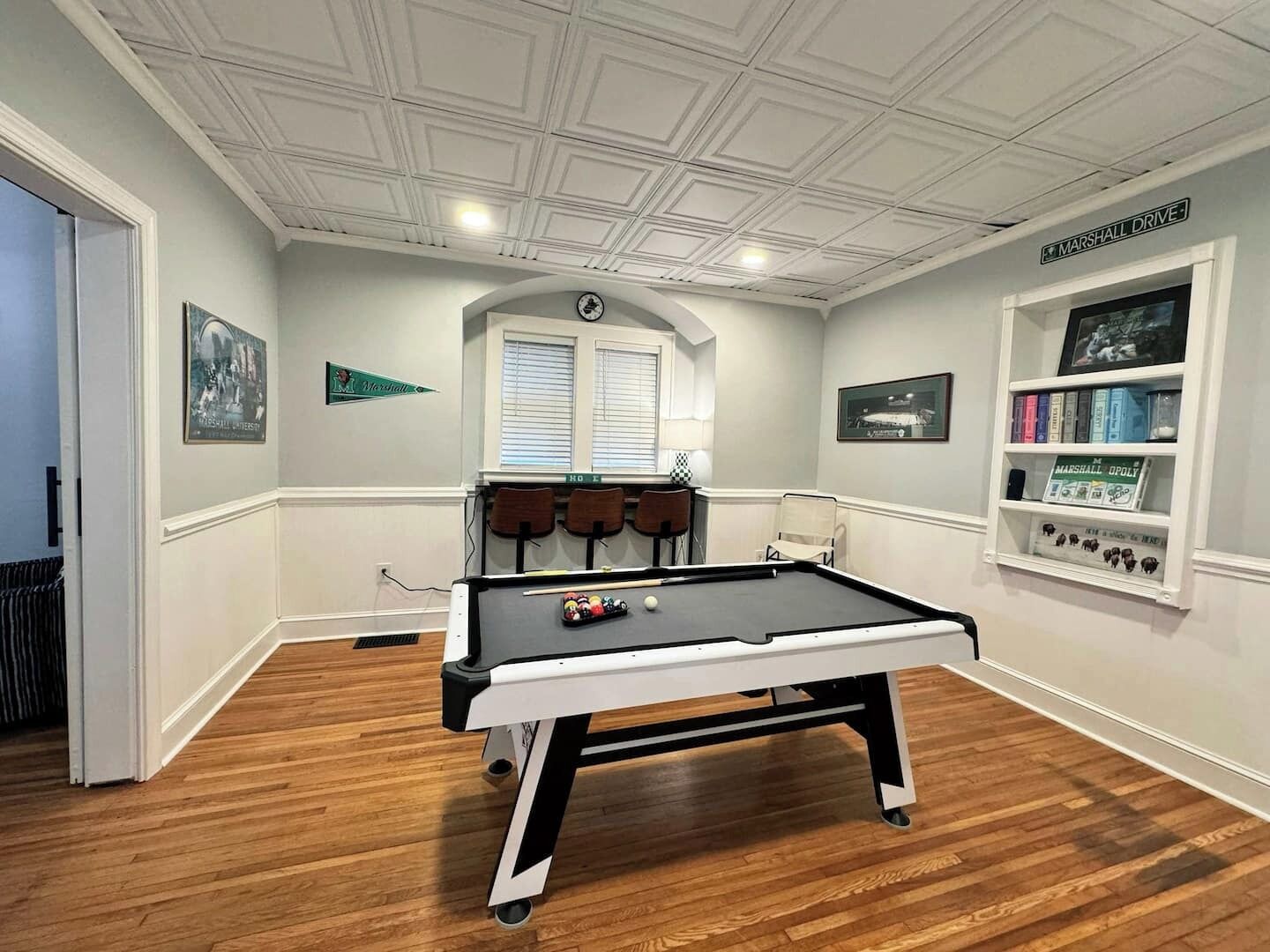 Une pièce avec une table de billard, une bibliothèque et une horloge au mur.