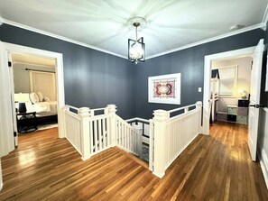 A hallway with wooden flooring, white railings, and a ceiling light fixture.