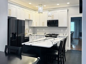 A modern kitchen with white cabinetry, a black refrigerator, a microwave, and a central island with bar stools.