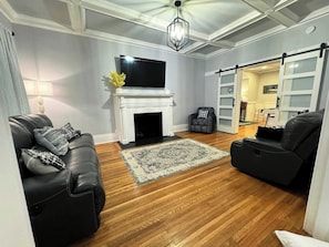 A living room with a fireplace, a flat-screen TV, and a sliding door leading to another room. - The Park House  A 5 Bedroom Retreat w/Game Room & (Huntington)