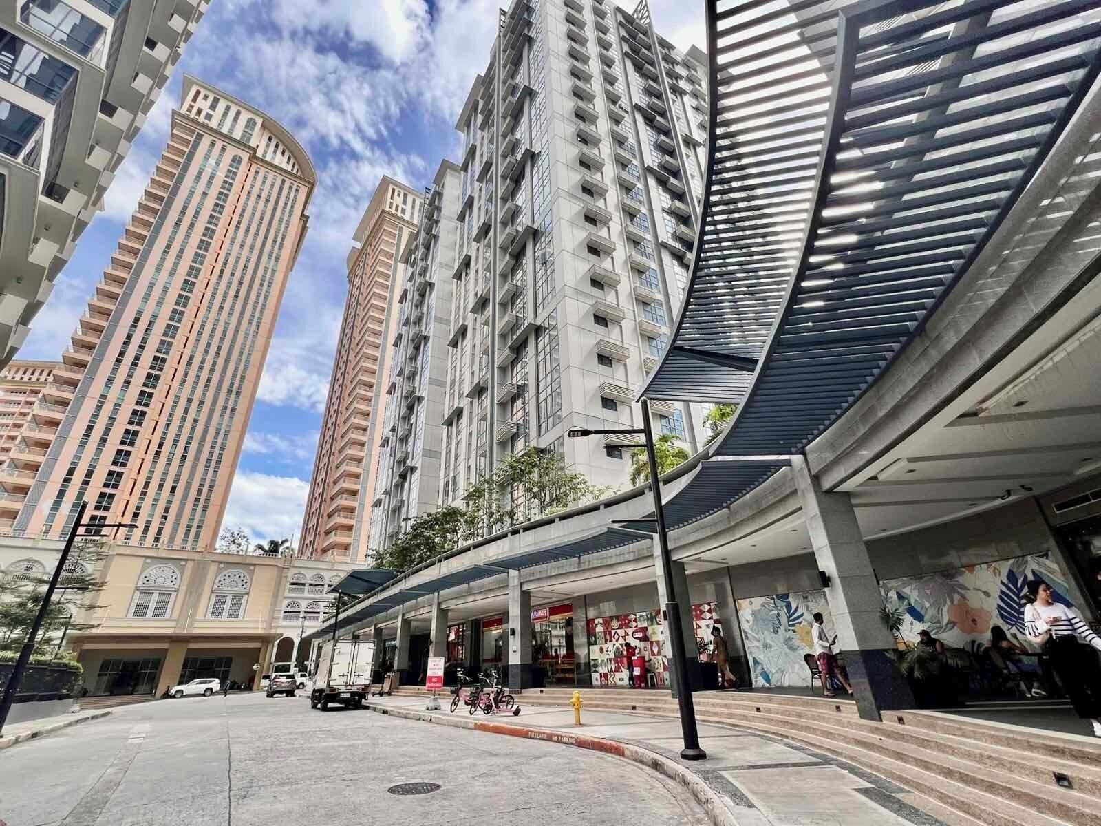 Una calle urbana moderna con edificios residenciales altos, un pasaje peatonal cubierto y una zona comercial con tiendas.