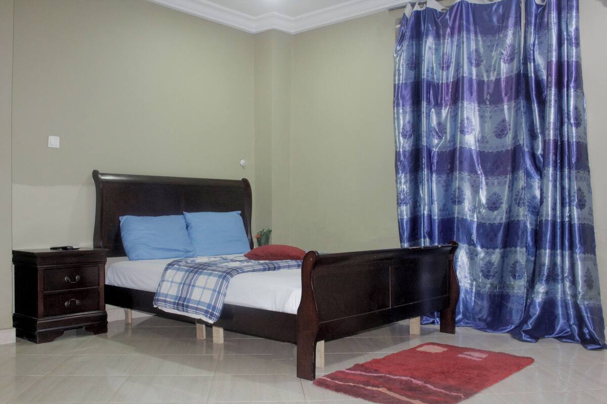 A bedroom with a wooden bed, a nightstand, a red rug, and a blue curtain.