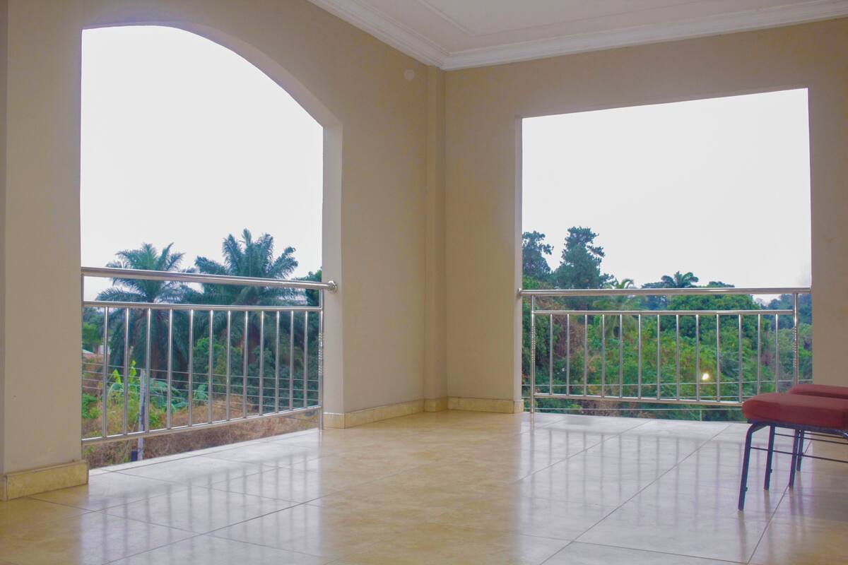 A spacious balcony with metal railings, a red bench, and a view of greenery and trees.
