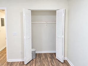 A walk-in closet with white sliding doors, a wooden floor, and a trash can.