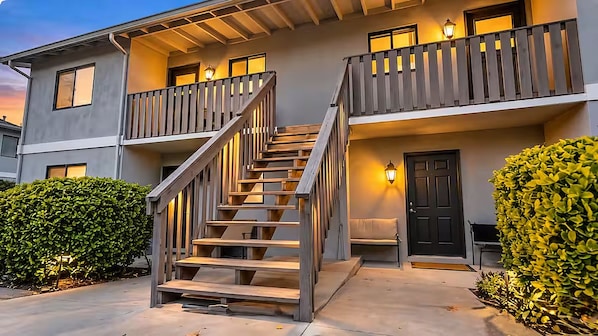 A two-story residential building with a wooden staircase, balconies, and exterior lighting.