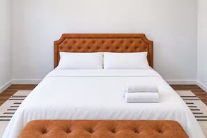 A neatly made bed with a tufted headboard, white bedding, and a matching ottoman.