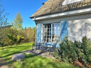 Une maison à l’extérieur bleu, avec un toit en tuiles et un jardin agrémenté d’une table et de chaises.