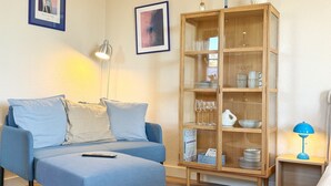 Una sala de estar moderna con un sofá azul, un mueble de madera con puertas de cristal y una mesita con una lámpara.