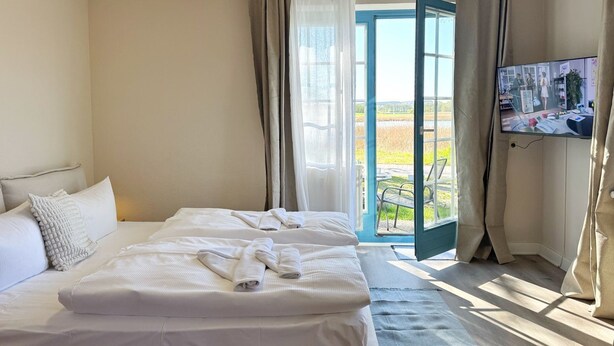 Habitación de hotel con una cama grande, televisión y vistas a un jardín a través de una puerta abierta.