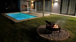 Un cortile con piscina, un braciere e una veranda coperta.