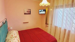 Un dormitorio con una cama, televisión y ventana con cortinas.