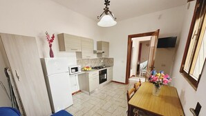 Cocina compacta con microondas, estufa y armarios. Hay una mesa de comedor con sillas y un florero.