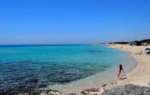 Ein Strand mit klarem türkisblauem Wasser, einem Sandstrand und einigen Personen.