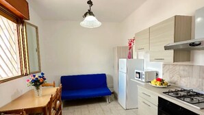 Cocina compacta con comedor, sofá azul y piso de baldosas.