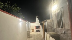 Ein überdachter Außenbereich mit Steinboden, an einer Seite eine weiße Wand und auf der anderen Seite ein Gebäude mit Kachelfassade.