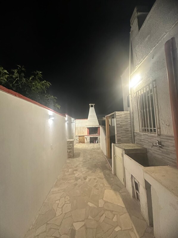 A stone-floored outdoor corridor with a white wall on one side and a building with a tiled facade on the other.
