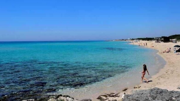 Ein Strand mit klarem türkisblauem Wasser, einem Sandstrand und einigen Personen.