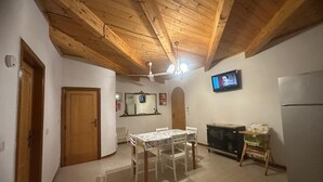 Eine Küche mit Holzbalken, einem Esstisch mit Stühlen, einem Kühlschrank, einem Fernseher und einem Schrank.