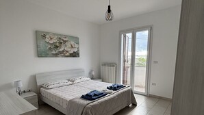 Ein Schlafzimmer mit Bett, Heizkörper, einem Gemälde, einer Lampe und Blick durch eine Glastür.