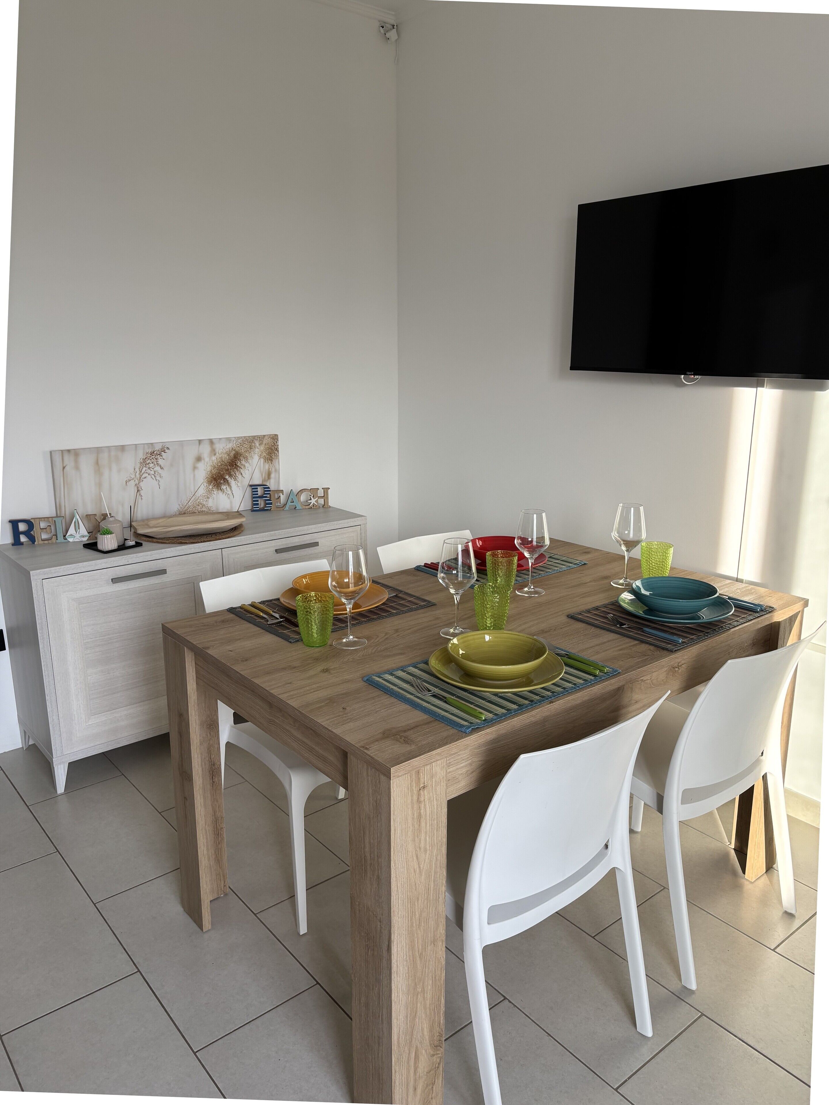A dining area with a wooden table, white chairs, and a flat-screen TV mounted on the wall.