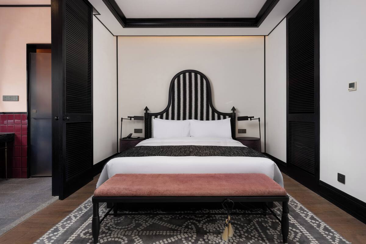 Quarto bem arrumado com cama grande, mesas de cabeceira e um banquinho.