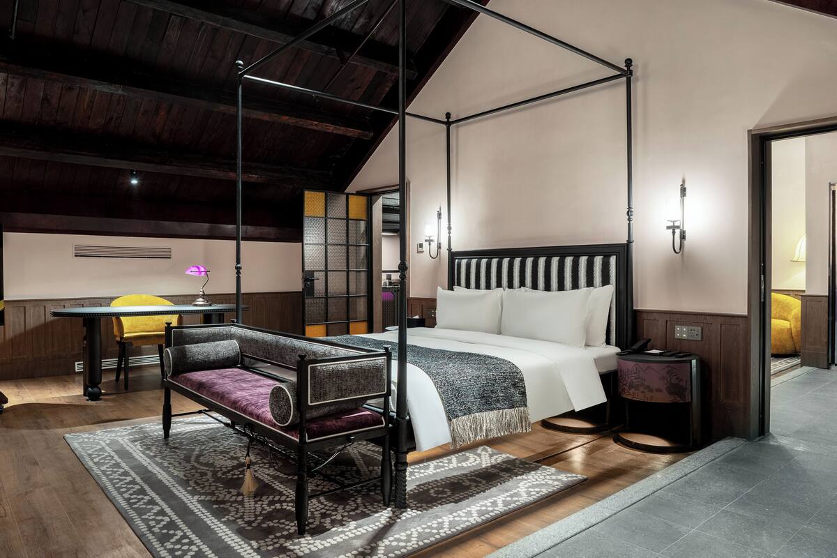 Uma cama de dossel com cabeceira branca e preta, uma mesa de cabeceira e um criado-mudo com uma luminária.
