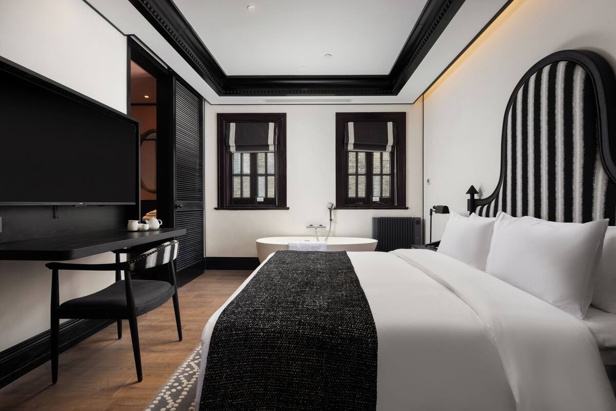 Quarto de hotel moderno com uma cama grande, uma escrivaninha e uma televisão.