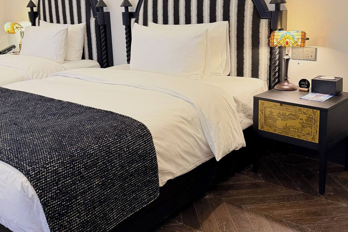 Uma cama bem arrumada com cabeceira listrada em preto e branco, uma mesa de cabeceira com abajur e uma caixa decorativa.