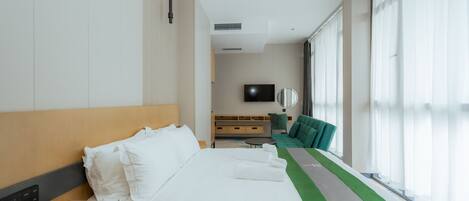 A hotel room with a bed, a bedside table, a TV, a sofa, and a large window.
