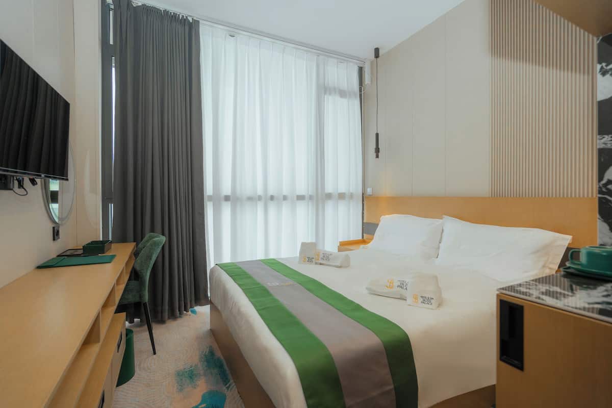 Hotelkamer met een bed, bureau, stoel, televisie en raam met gordijnen.