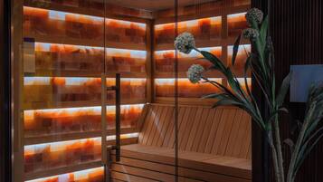 A modern sauna with a glass door, wooden interior, and a potted plant.