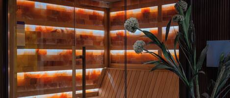 Una sauna moderna con puerta de cristal, interior de madera y una planta en maceta.