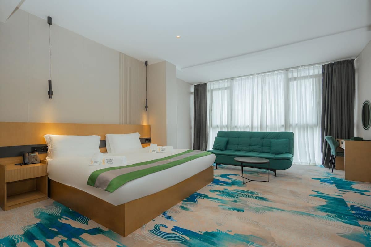 Een moderne hotelkamer met een groot bed, een groene bank, een kleine tafel en een bureau.