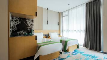 A hotel room with two beds, a kitchenette, a large window with curtains, and a patterned carpet.