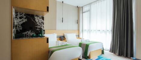 Habitación de hotel con dos camas, kitchenette, ventana grande con cortinas y alfombra estampada.