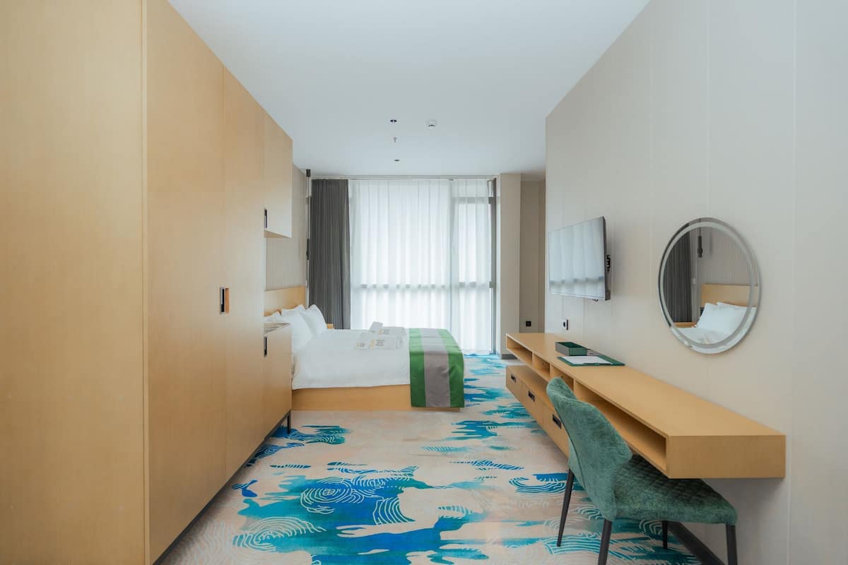 Een hotelkamer met een bed, bureau, stoel, televisie en spiegel.