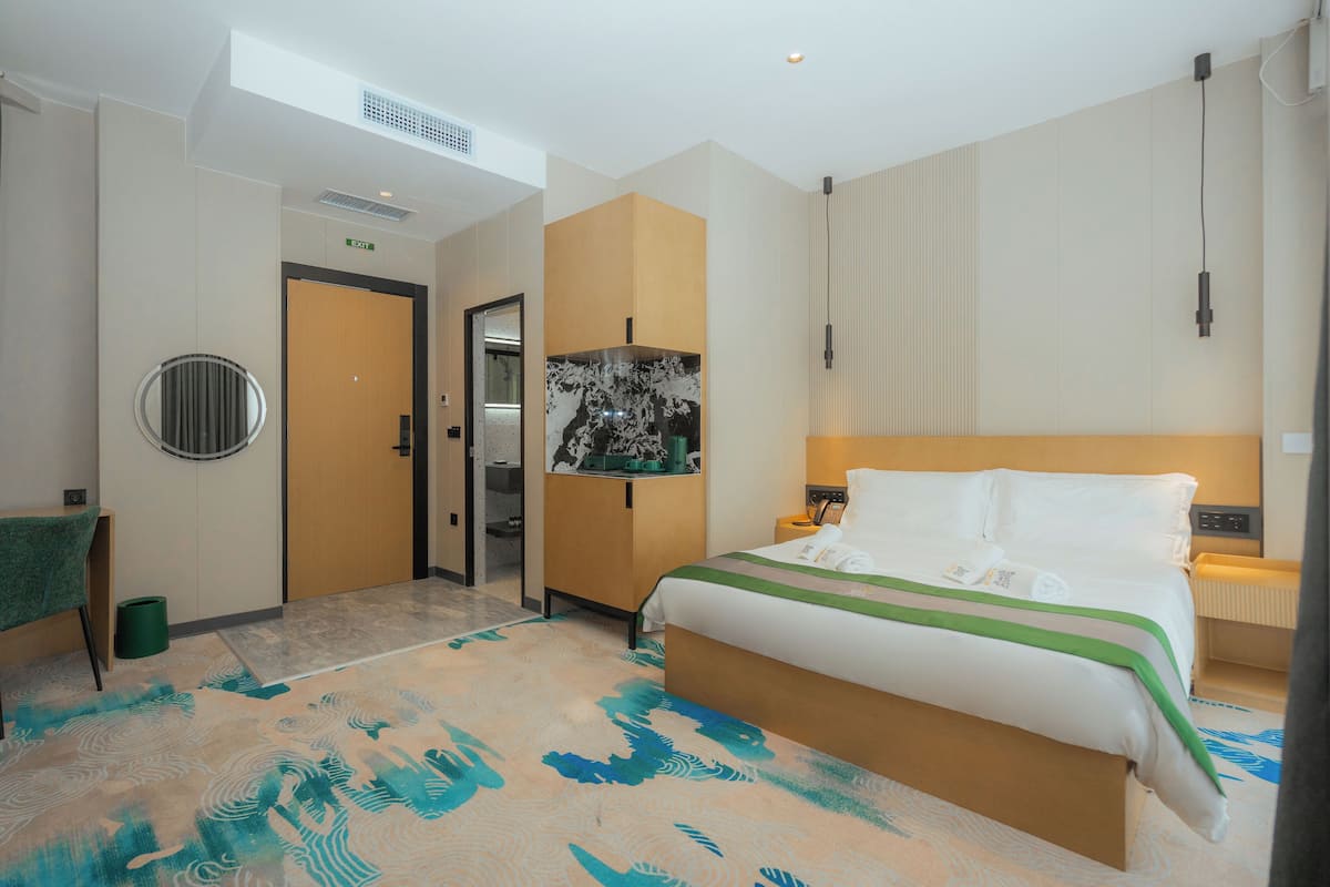 Een hotelkamer met een groot bed, een bureau, een stoel, een prullenbak en een deur.