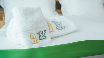 Un lit bien fait, avec des oreillers blancs et une couvre-lit verte. Chaque oreiller est agrémenté d’une serviette blanche sur laquelle est brodé le texte « HOTEL & SPA BLISS PALACE ».