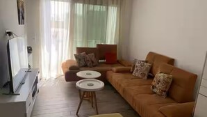 A living room with a sofa, two small round tables, a TV, and a yellow ottoman. - Chic Luxury Duplex in The Heart ofla Marsa - Walk to Beach and Cafés (Marsa)