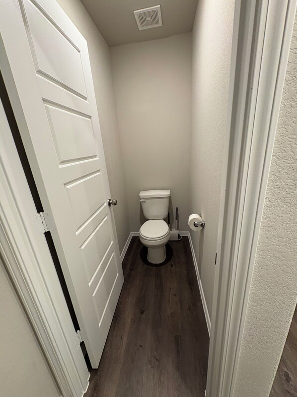 A small, narrow bathroom with a white toilet, a wooden floor, and white walls.
