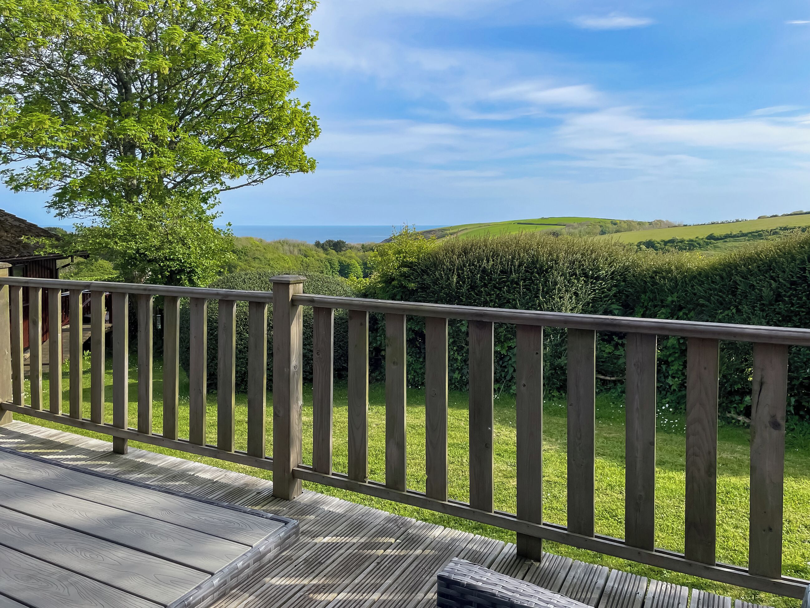 Eine Holzdielen-Terrasse mit Blick auf grüne Hügel und einen klaren Himmel.