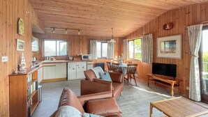A cozy cabin interior with a wooden interior, a dining area, and a living room with a sofa and a television. - 3 bedroom accommodation in Portscatho (Portscatho)