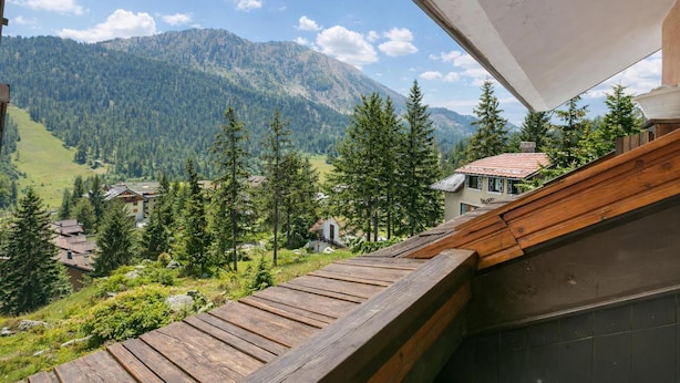 Een houten terras met uitzicht op een bergachtig landschap, inclusief huizen en bomen.