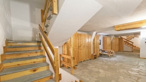 Een trap met houten treden en een leuning, leidend naar een kamer met houten kasten en een vloer met een stenen patroon.