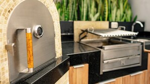 A modern kitchen with a built-in pizza oven, a stainless steel range, and a black countertop. - Beautiful and Well Located (Miraflores)