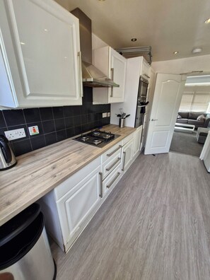 A modern kitchen with white cabinetry, a wooden countertop, and a black tiled backsplash.
