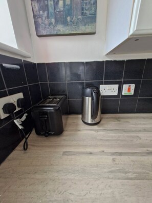 A kitchen with a toaster, kettle, and a painting on the wall.