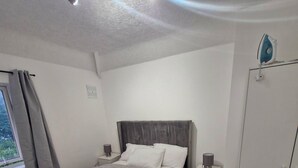 A bedroom with a bed, bedside tables, a wardrobe, and a window with curtains. - Cosy 3-Bed Home  close to city and shops (Coventry)